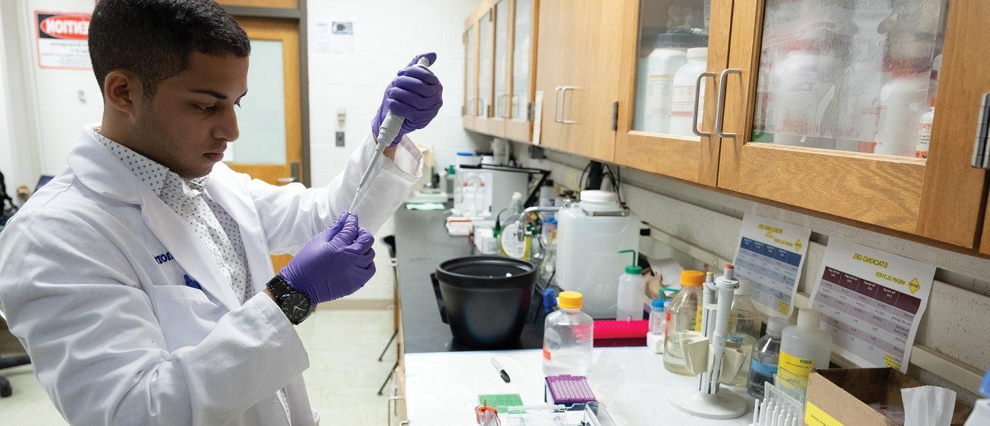 A man wearing a white lab coat, holding a medical syringe in a medical lab.